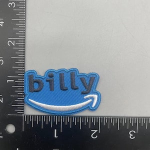 Pode incluir: Patch bordado azul e branco com a palavra "billy" em letras pretas e um logotipo da Amazon branco.