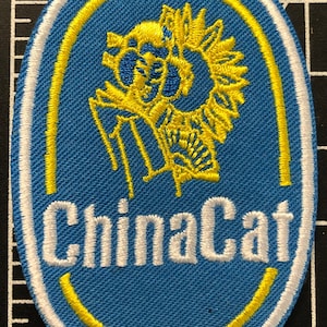 May include: A blue and yellow oval embroidered patch with the text "ChinaCat" in white lettering. The patch features a stylized yellow cat design.