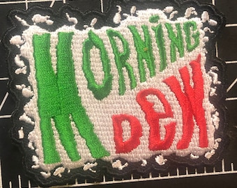 May include: A white, green, and red embroidered patch with the words "MORNING DEW" in a stylized font. The patch has a black, jagged border.