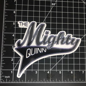 May include: Black and white sticker with the text "The Mighty Quinn" in a white, black, and blue baseball-style font.