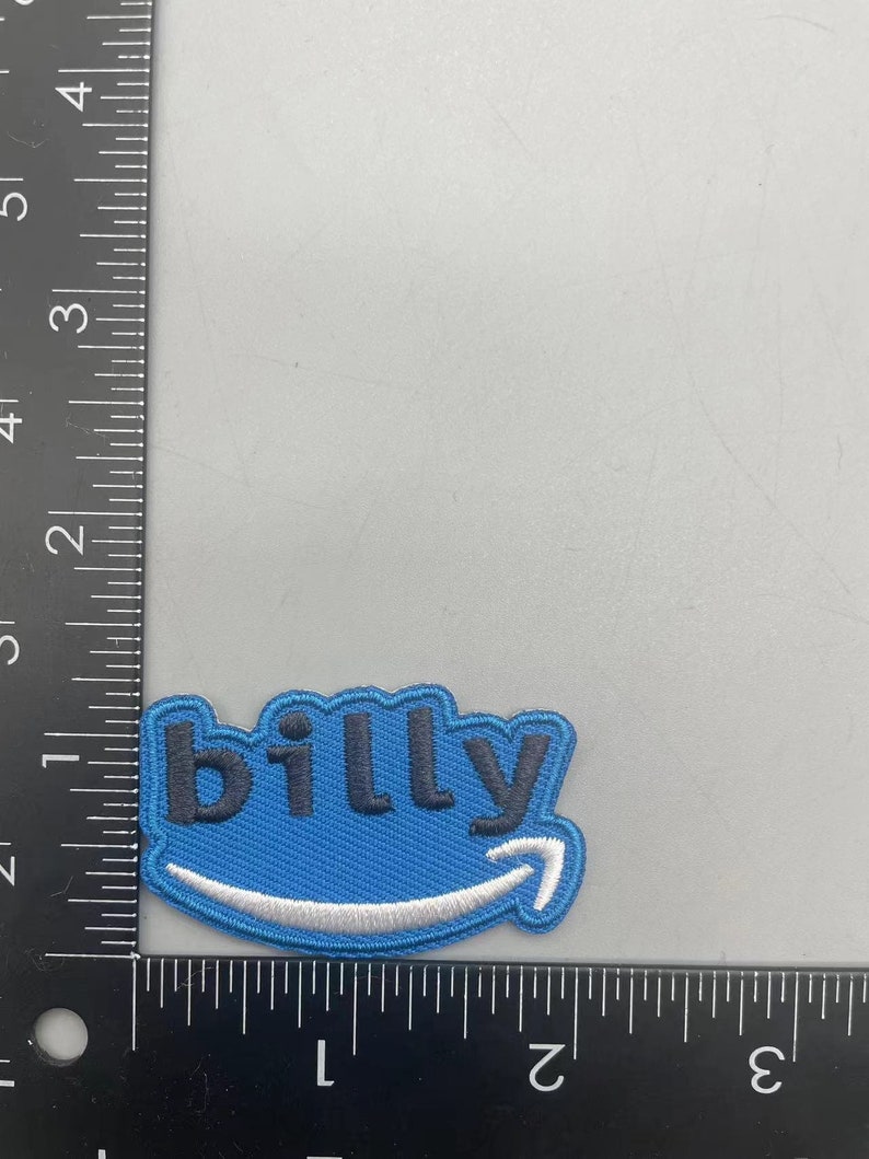 Pode incluir: Patch bordado azul e branco com a palavra "billy" em letras pretas e um logotipo da Amazon branco.
