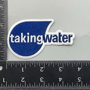 May include: A blue and white embroidered patch with the text "taking water" in white lettering.