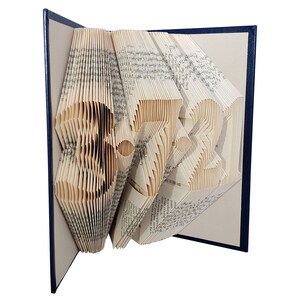 Puede incluir: Una escultura de arte de libro con forma de n&uacute;mero 3721. El libro est&aacute; doblado y las p&aacute;ginas son de color crema. El libro est&aacute; encuadernado en una cubierta azul oscuro.