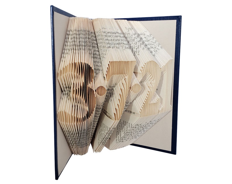 Puede incluir: Una escultura de arte de libro con forma de n&uacute;mero 3721. El libro est&aacute; doblado y las p&aacute;ginas son de color crema. El libro est&aacute; encuadernado en una cubierta azul oscuro.
