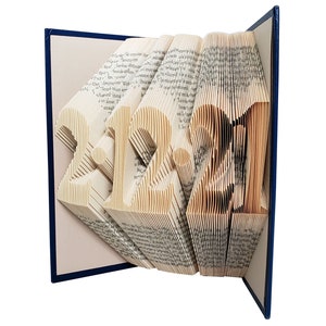Puede incluir: Un libro con las p&aacute;ginas dobladas para crear una escultura tridimensional de los n&uacute;meros "2021". El libro est&aacute; encuadernado en azul y tiene una cubierta blanca.