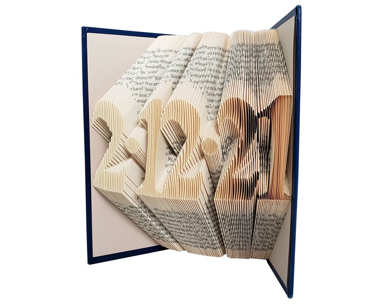 Puede incluir: Un libro con las p&aacute;ginas dobladas para crear una escultura tridimensional de los n&uacute;meros "2021". El libro est&aacute; encuadernado en azul y tiene una cubierta blanca.