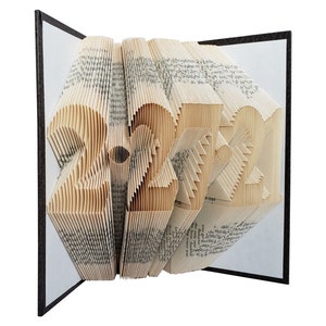 Puede incluir: Una escultura de arte de libro con forma de n&uacute;mero 2021. El libro est&aacute; hecho de p&aacute;ginas que se han doblado y superpuesto para crear un dise&ntilde;o tridimensional. La escultura est&aacute; hecha de un libro vintage con una cubierta marr&oacute;n.