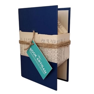 Puede incluir: Un libro azul marino con una etiqueta blanca que dice "The Book Artisan" est&aacute; envuelto en cuerda y tiene p&aacute;ginas dobladas en un dise&ntilde;o 3D.