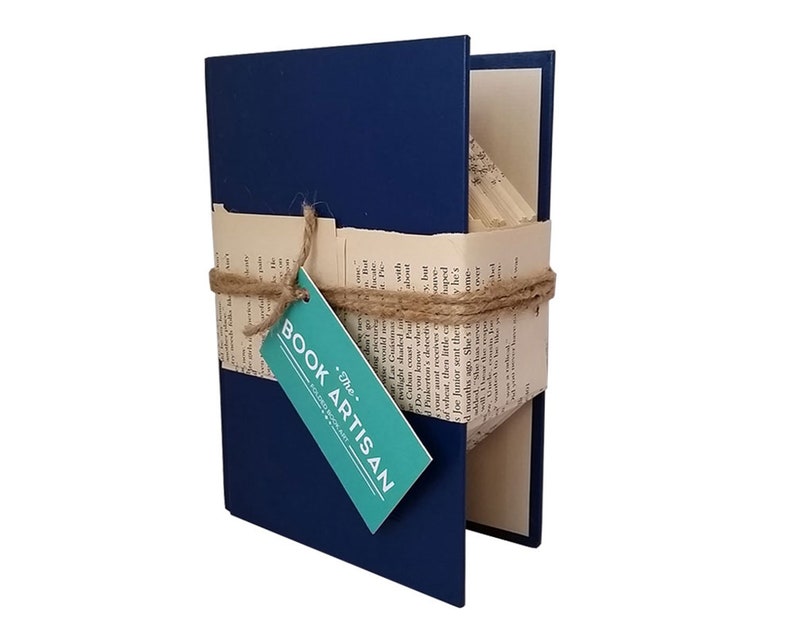 Puede incluir: Un libro azul marino con una etiqueta blanca que dice "The Book Artisan" est&aacute; envuelto en cuerda y tiene p&aacute;ginas dobladas en un dise&ntilde;o 3D.