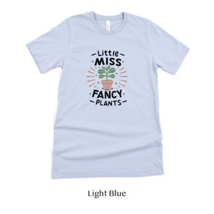 May include: Light blue t-shirt with a graphic of a potted plant and the text "Little Miss Fancy Plants".