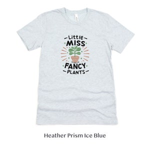 May include: A light blue t-shirt with the text "Little Miss Fancy Plants" and a graphic of a potted plant with green leaves.