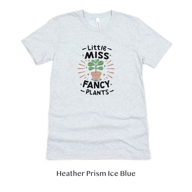 May include: A light blue t-shirt with the text "Little Miss Fancy Plants" and a graphic of a potted plant with green leaves.