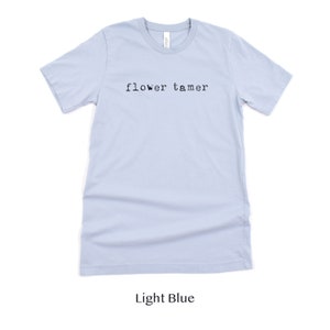 May include: Light blue t-shirt with the text "flower tamer" printed in black.