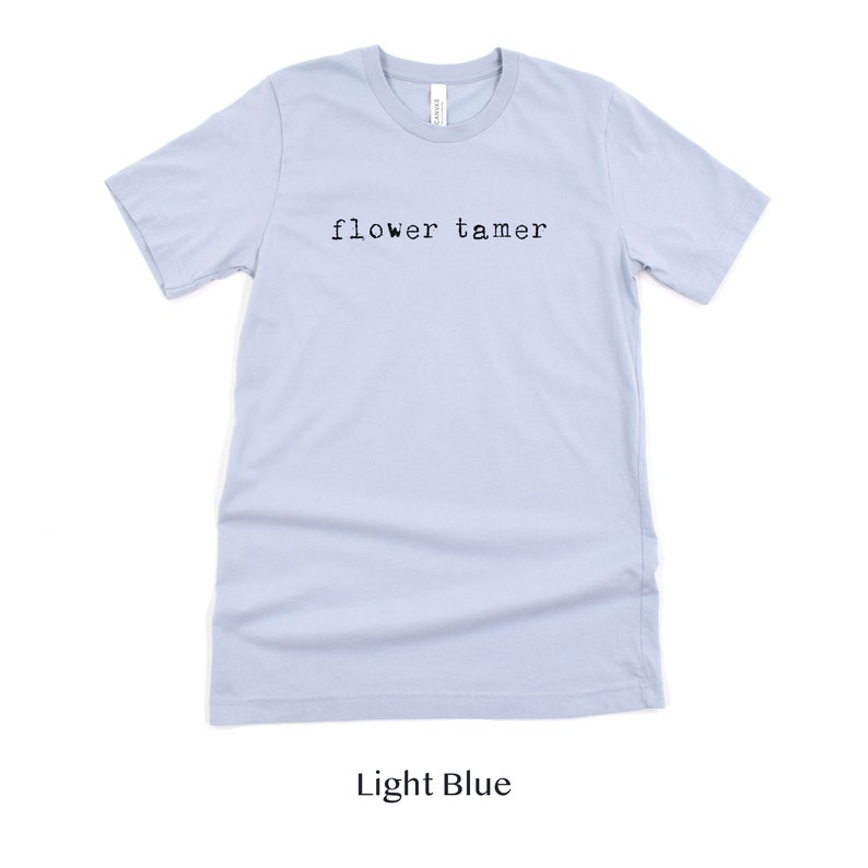 May include: Light blue t-shirt with the text "flower tamer" printed in black.