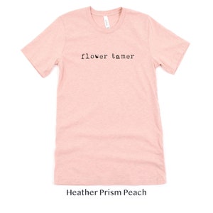 May include: A heather prism peach t-shirt with the text "flower tamer" printed in black.