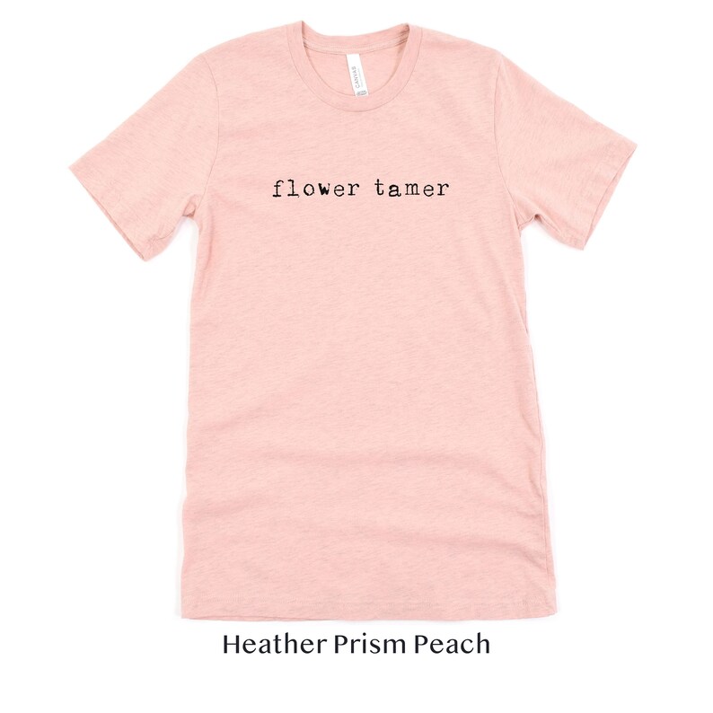 May include: A heather prism peach t-shirt with the text "flower tamer" printed in black.