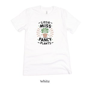 May include: White t-shirt with a graphic of a potted plant and the text "Little Miss Fancy Plants".