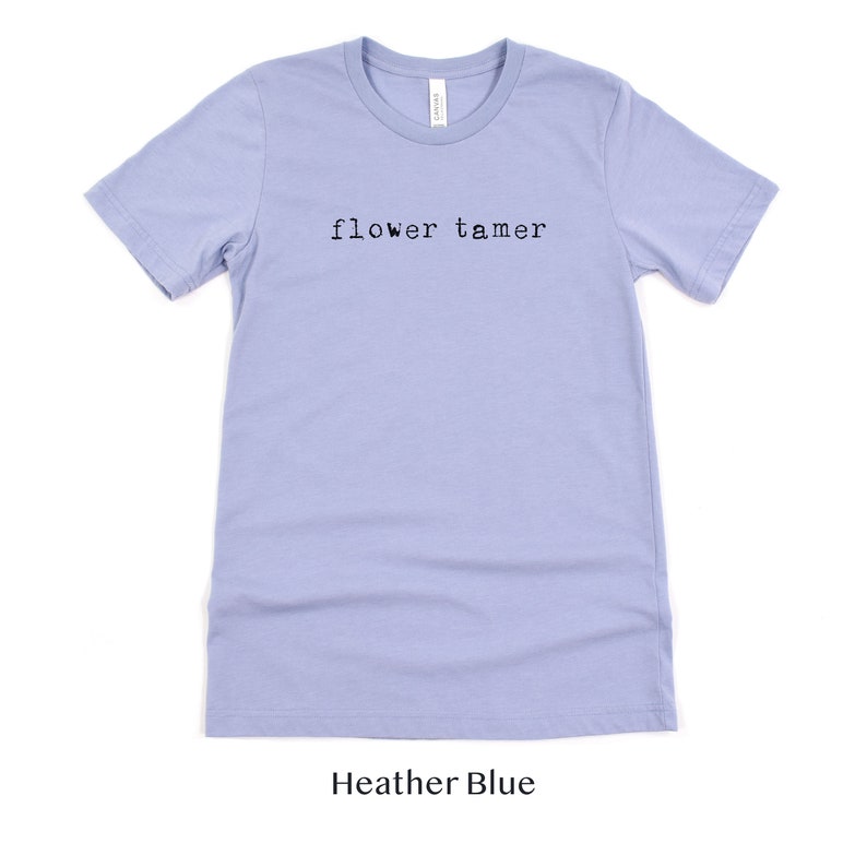 May include: A light blue t-shirt with the text "flower tamer" printed in black on the front. The shirt is made of a soft, comfortable material.