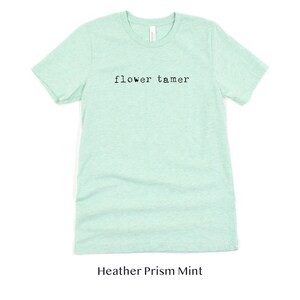 May include: A light green t-shirt with the text "flower tamer" printed on the front. The shirt is made of a soft, comfortable material and is perfect for everyday wear.
