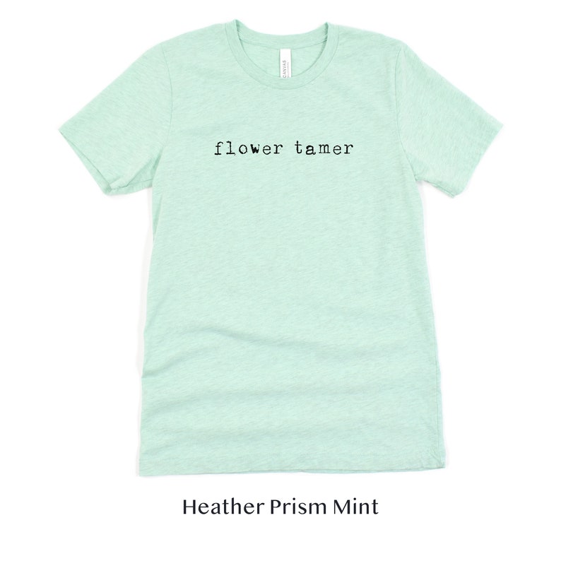 May include: A light green t-shirt with the text "flower tamer" printed on the front. The shirt is made of a soft, comfortable material and is perfect for everyday wear.