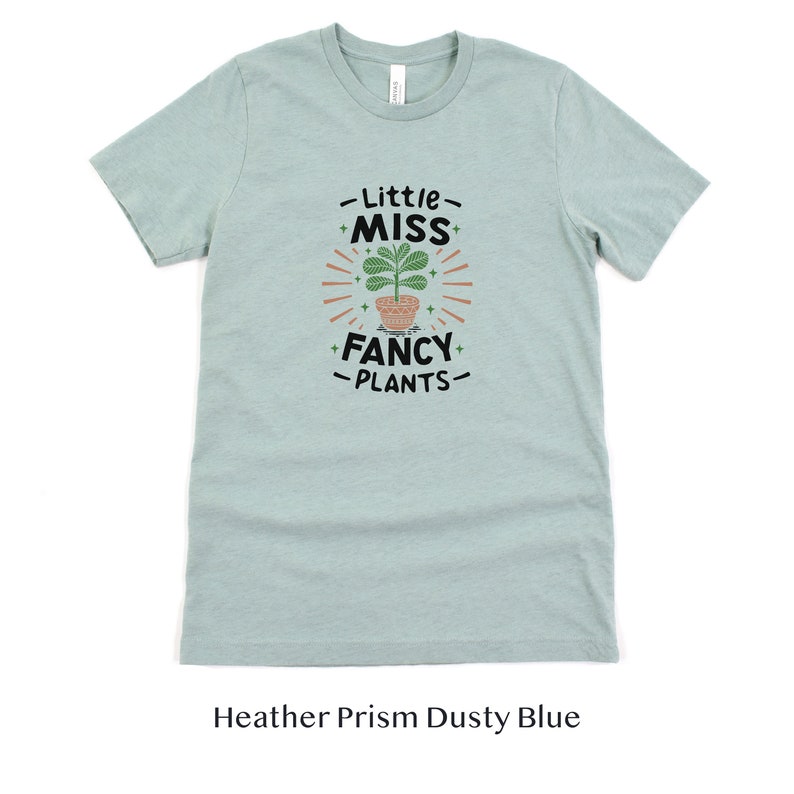 May include: A light blue t-shirt with the text "Little Miss Fancy Plants" and a graphic of a potted plant with green leaves.