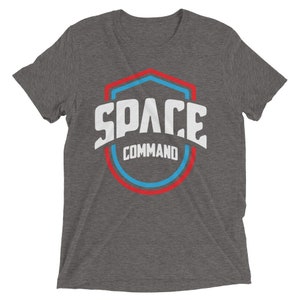 May include: A heather grey t-shirt with a white graphic of a red, blue, and white shield with the text "SPACE COMMAND" inside.