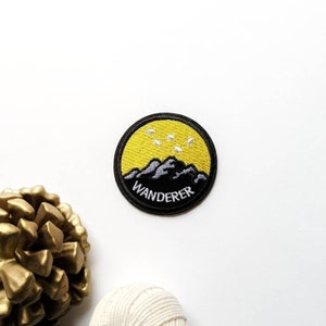 May include: A black and yellow embroidered patch with a mountain range and stars. The text "WANDERER" is embroidered in white on the patch.