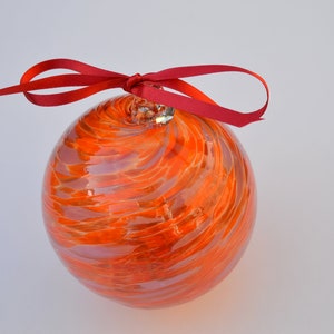 Può includere: Addobbo di vetro arancione con un motivo a spirale e un nastro rosso legato in cima.