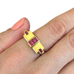 May include: A gold ring with three rectangular ruby stones set in a geometric design.