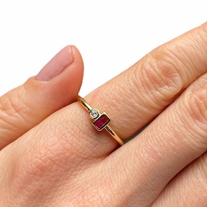May include: A gold ring featuring a small red rectangular stone and a smaller round clear stone.