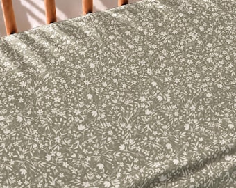 May include: A fitted sheet featuring a repeating pattern of small white flowers and delicate leaves set against a muted sage green background. The fabric is stretched taut over a wooden frame, displaying a dense botanical print across the surface.