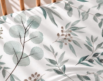 May include: A white fitted sheet featuring a watercolour botanical print of eucalyptus branches, olive sprigs, and small brown berries in shades of sage green, muted teal, and dark olive, displayed on a wooden crib frame.