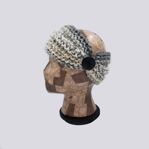 May include: A gray, white, and black knit headband with a black button. The headband is on a mannequin head.