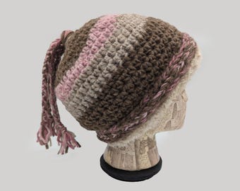 May include: A brown, beige, and pink crocheted hat with a long, braided tail. The hat has a fluffy white lining.