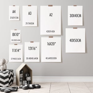 May include: A white wall with eight different sized paper frames, each with a different measurement in inches and centimeters. The frames are hung on the wall in a staggered pattern. The frames are all white and have a simple, modern design.