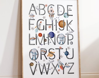 May include: A white poster with a gray alphabet printed on it. Each letter is decorated with space-themed illustrations, including rockets, planets, stars, and astronauts. The poster is framed in a light wood frame.