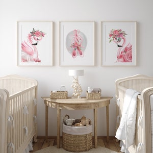 May include: Three pink framed prints featuring watercolour illustrations of pink flamingos with floral headbands and pink ballet shoes. The prints are hanging on a white wall above a wooden table with a wicker basket filled with soft toys.