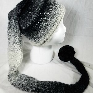 May include: A black and white ombre crochet hat with a long, matching tail and a black pom-pom at the end.
