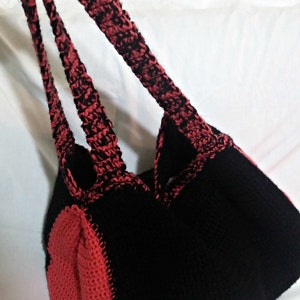 May include: A black and red crocheted tote bag with two straps. The bag is made with a textured stitch and has a heart-shaped design on the bottom.