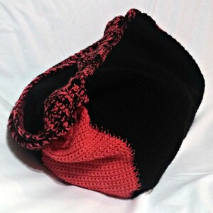 May include: A black and red crocheted tote bag with a contrasting color design. The bag is made of soft yarn and has a spacious interior.