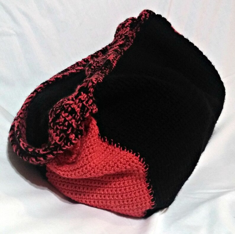 May include: A black and red crocheted tote bag with a contrasting color design. The bag is made of soft yarn and has a spacious interior.