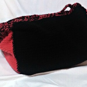 May include: A black and red crocheted tote bag with a single handle. The bag is made of thick yarn and has a textured surface.