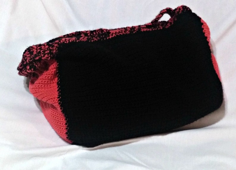 May include: A black and red crocheted tote bag with a single handle. The bag is made of thick yarn and has a textured surface.