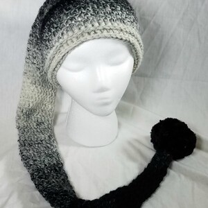 May include: A black and white ombre crocheted hat with a long tail and a black pom pom at the end.
