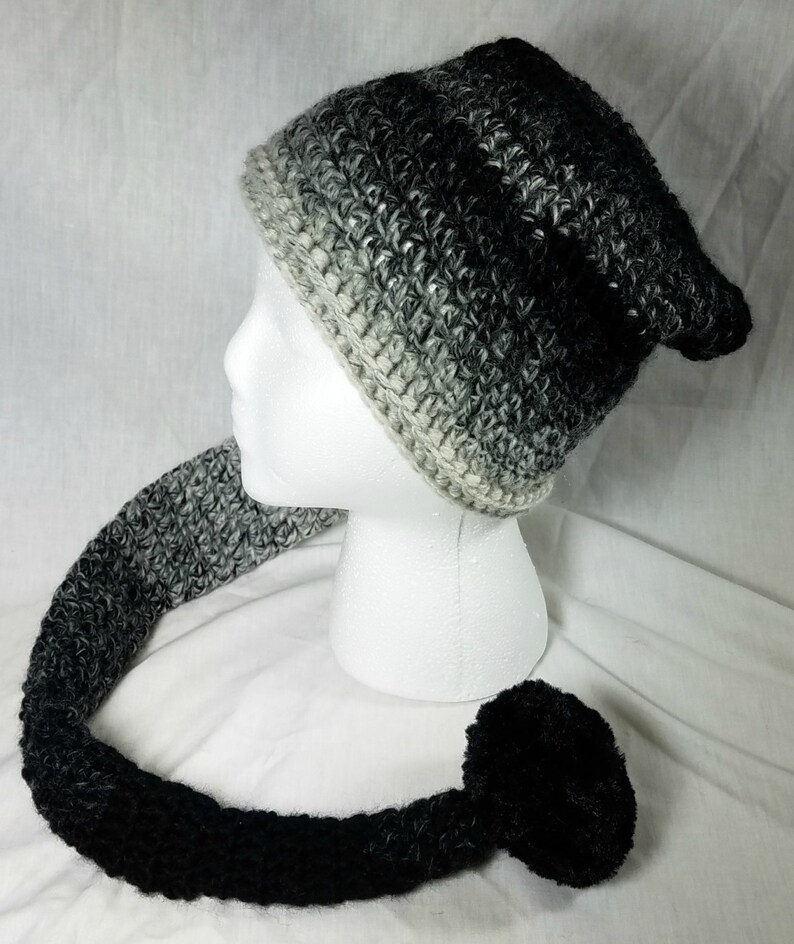 May include: A black and white ombre crocheted beanie with a long, matching tail and a black pom-pom.