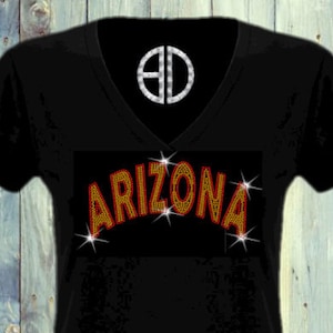 May include: Black v-neck t-shirt with a rhinestone design that says "ARIZONA" in orange and gold. The shirt is by @Blingdots.