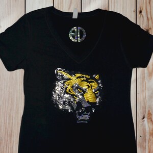 May include: Black v-neck t-shirt with a rhinestone tiger head design. The tiger is yellow and silver with a black background. The shirt has a monogram on the chest that says "AD".