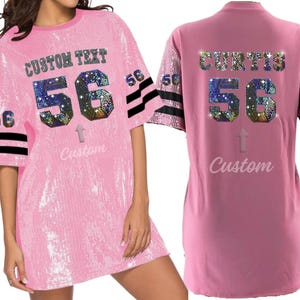 Puede incluir: Vestido de jersey rosa con lentejuelas y rayas negras y blancas en las mangas. La parte delantera del vestido tiene el texto "CUSTOM TEXT" y el n&uacute;mero "56" en pedrer&iacute;a. La parte trasera del vestido tiene el texto "CURTIS" y el n&uacute;mero "56" en pedrer&iacute;a.