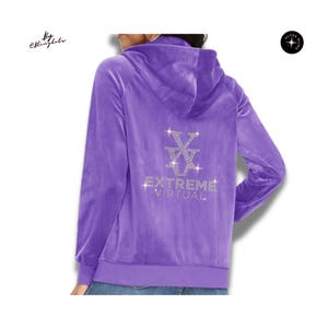May include: A purple velour zip-up hoodie featuring a hood and long sleeves. The back displays a rhinestone-embellished logo consisting of a stylized V-shaped emblem above the text "EXTREME VIRTUAL" in clear, sparkling crystals.