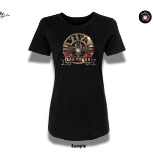 Könnte beinhalten: Ein schwarzes T-Shirt mit kurzen Ärmeln und einem zentralen Grafikdesign mit dem Text Viva Las Vegas und Rockabilly Weekend. Das Design enthält goldene und rote Akzente mit glitzerndem Finish. Ein kleines kreisförmiges Logo zeigt Ultra Bling.